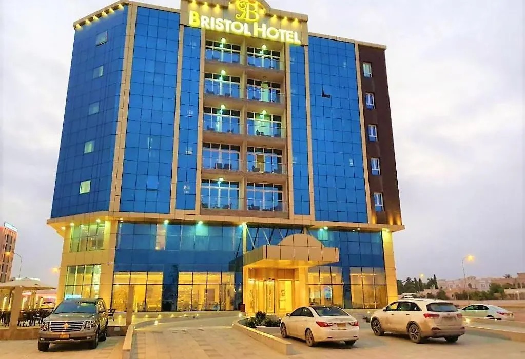 Bristol Hotel Salalah at dusk: a blue glass tower with the hotel name lit on the roof